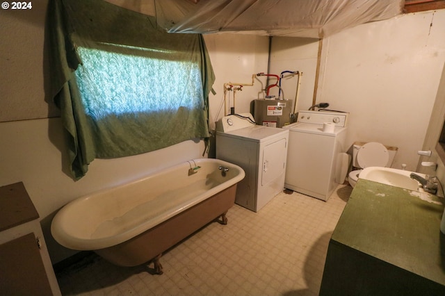 bathroom featuring washing machine and clothes dryer, a tub, sink, electric water heater, and toilet