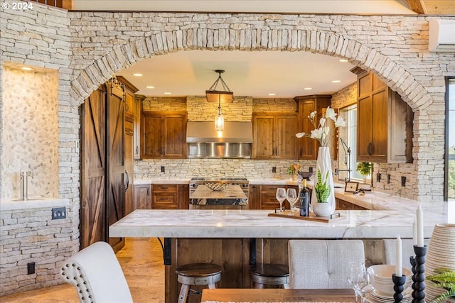 kitchen featuring backsplash, hanging light fixtures, wall chimney exhaust hood, stainless steel range, and a breakfast bar area