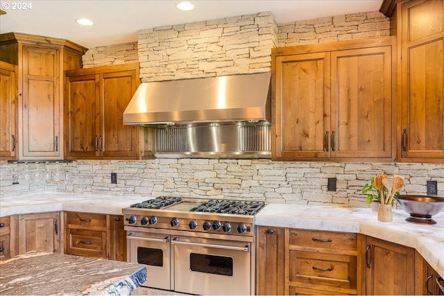 kitchen with double oven range, wall chimney range hood, and tasteful backsplash