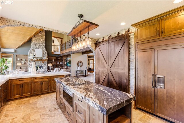 kitchen featuring a barn door, a wall unit AC, built in appliances, dark stone counters, and a kitchen island