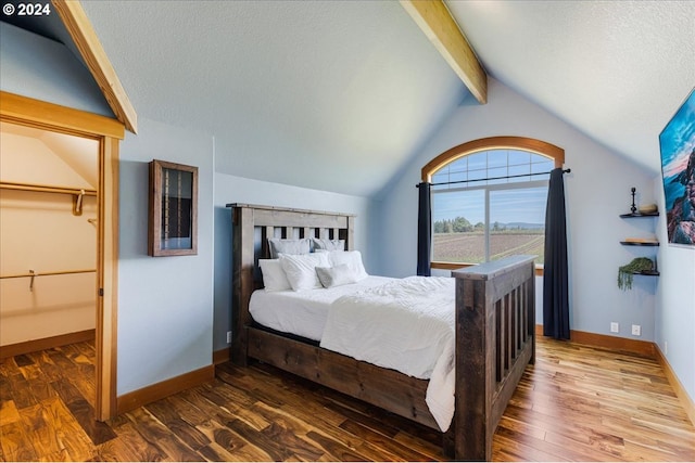 bedroom with hardwood / wood-style flooring, lofted ceiling with beams, a spacious closet, and a textured ceiling