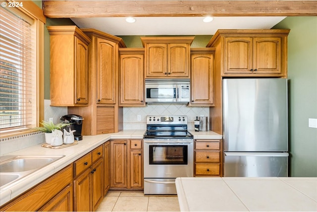 kitchen featuring tile counters, sink, stainless steel appliances, decorative backsplash, and light tile patterned floors