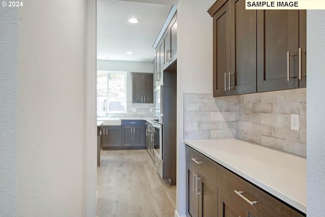 kitchen with tasteful backsplash, a textured ceiling, dark brown cabinetry, sink, and light hardwood / wood-style flooring