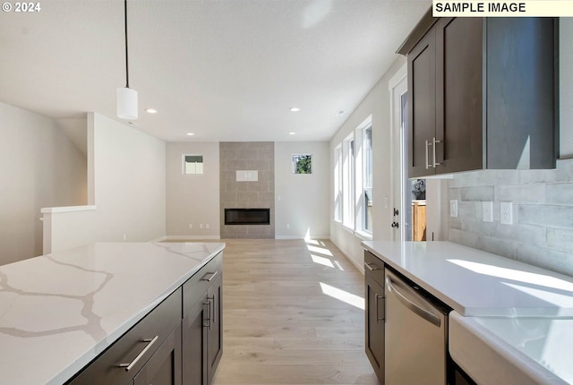 kitchen featuring a tile fireplace, light stone countertops, hanging light fixtures, light hardwood / wood-style flooring, and stainless steel dishwasher