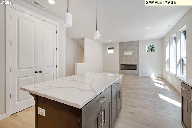 kitchen with light stone countertops, light wood-type flooring, dark brown cabinetry, a fireplace, and hanging light fixtures