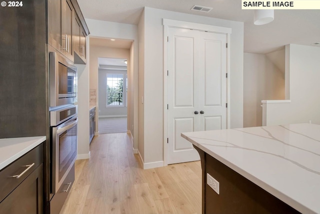 kitchen with light wood-type flooring, stainless steel appliances, light stone counters, and dark brown cabinetry