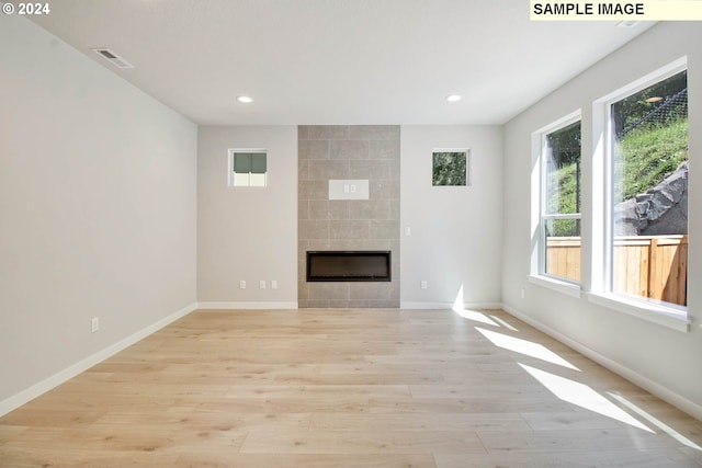 unfurnished living room with a tile fireplace and light hardwood / wood-style flooring