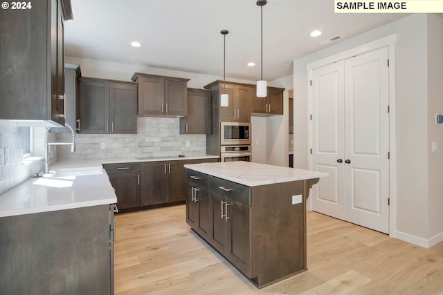 kitchen with pendant lighting, a center island, stainless steel appliances, and light hardwood / wood-style flooring