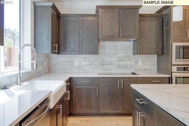 kitchen with backsplash, sink, light wood-type flooring, light stone countertops, and stainless steel appliances