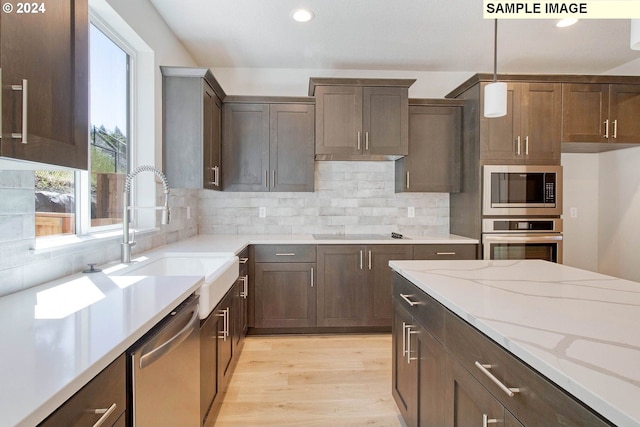 kitchen featuring light stone countertops, appliances with stainless steel finishes, light wood-type flooring, tasteful backsplash, and decorative light fixtures