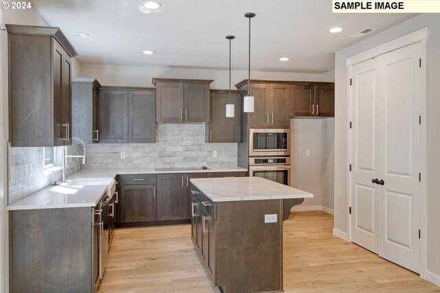 kitchen with appliances with stainless steel finishes, light wood-type flooring, a kitchen island, and sink