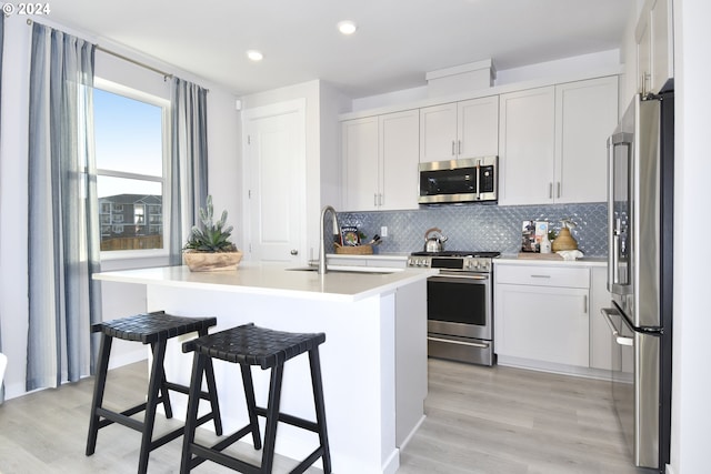 kitchen featuring appliances with stainless steel finishes, light hardwood / wood-style flooring, white cabinetry, and an island with sink