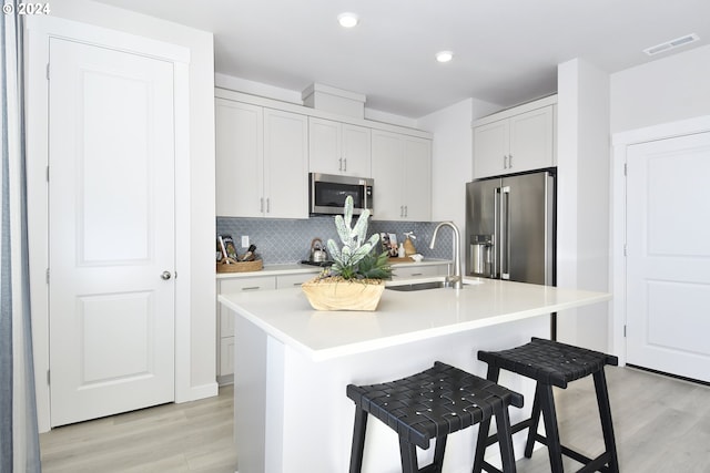 kitchen with a kitchen bar, stainless steel appliances, sink, a center island with sink, and white cabinets