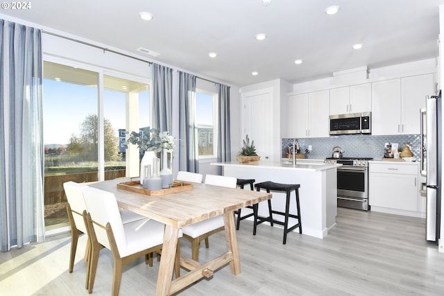 kitchen with a center island with sink, light hardwood / wood-style flooring, appliances with stainless steel finishes, tasteful backsplash, and white cabinetry