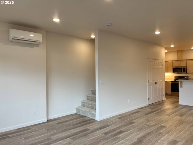 unfurnished living room with stairway, a wall mounted AC, light wood-type flooring, baseboards, and recessed lighting