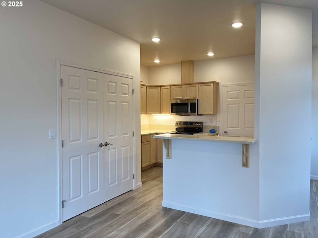 kitchen with a peninsula, a kitchen breakfast bar, light countertops, appliances with stainless steel finishes, and light wood finished floors