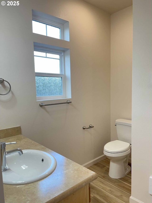 bathroom featuring baseboards, wood finished floors, toilet, and vanity