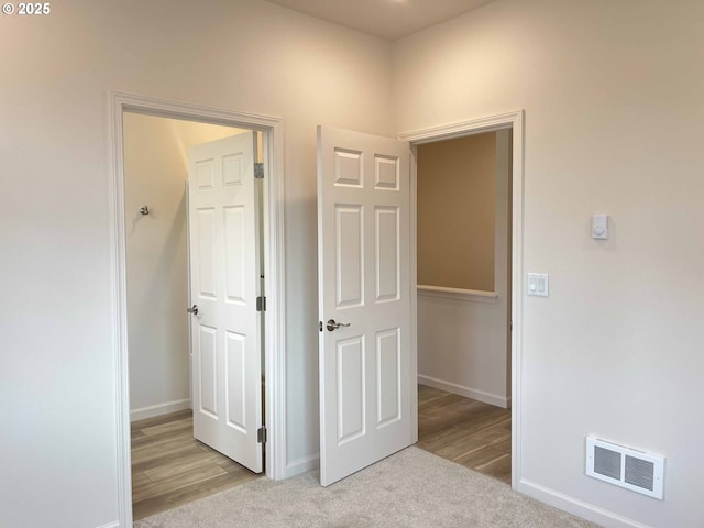 hall with baseboards, visible vents, and light colored carpet