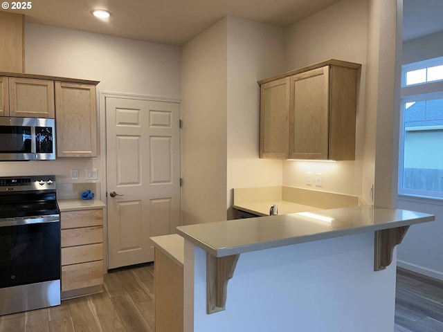kitchen featuring light countertops, wood finished floors, a peninsula, a kitchen bar, and appliances with stainless steel finishes