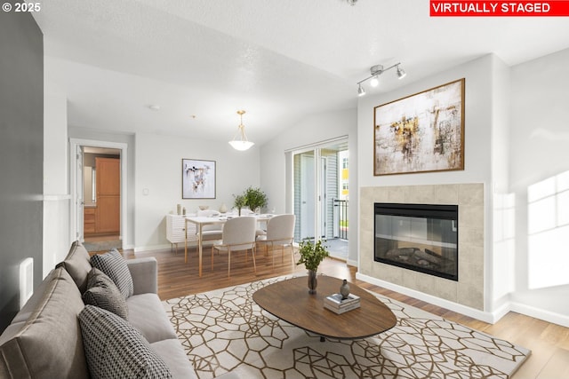 living room with vaulted ceiling, light hardwood / wood-style flooring, and a tiled fireplace