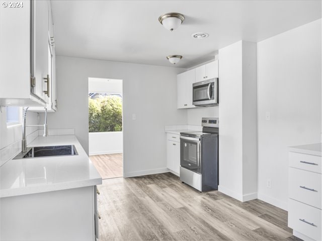 kitchen with sink, appliances with stainless steel finishes, light wood-type flooring, and white cabinetry