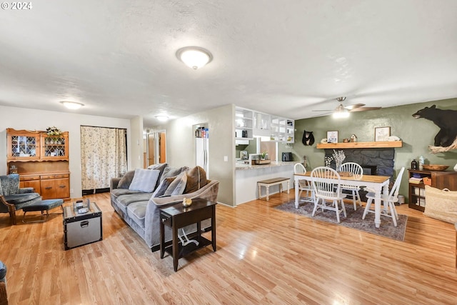 living room with a fireplace, ceiling fan, and light wood-type flooring