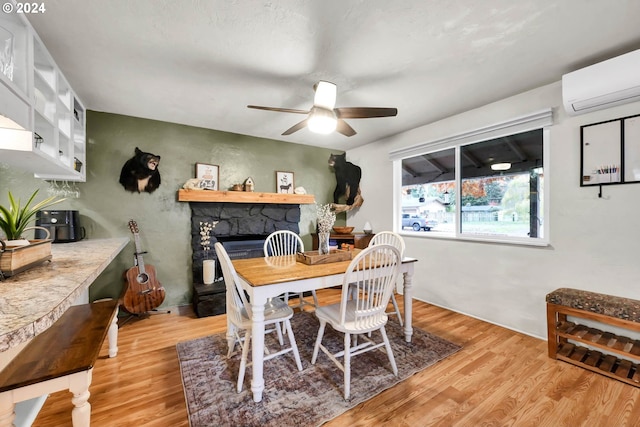 dining space featuring ceiling fan, a fireplace, a wall mounted AC, and light wood-type flooring