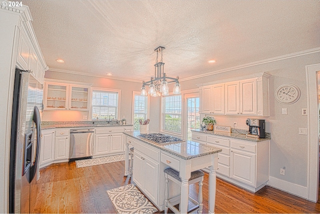 kitchen with light wood-type flooring, appliances with stainless steel finishes, light stone counters, and white cabinets