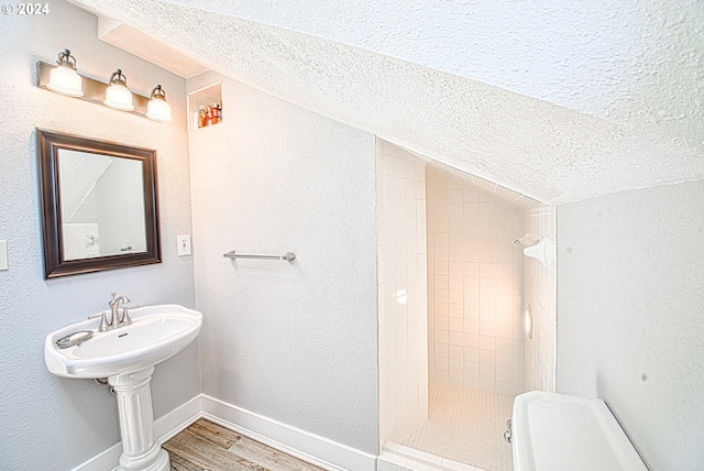 bathroom with toilet, hardwood / wood-style floors, a textured ceiling, a tile shower, and vaulted ceiling