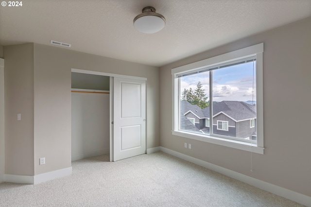 unfurnished bedroom with light carpet, a textured ceiling, and a closet