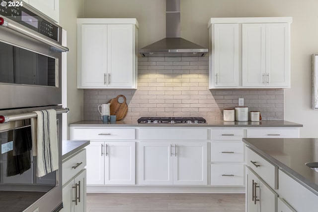 kitchen featuring wall chimney exhaust hood, white cabinets, appliances with stainless steel finishes, and light hardwood / wood-style flooring