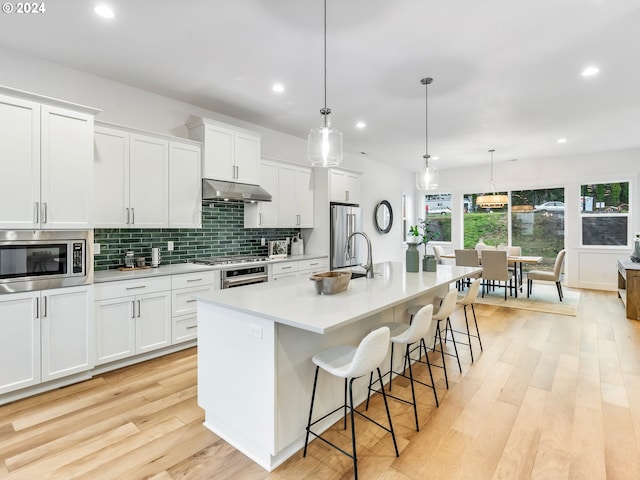 kitchen featuring white cabinetry, stainless steel appliances, an island with sink, decorative light fixtures, and a kitchen bar