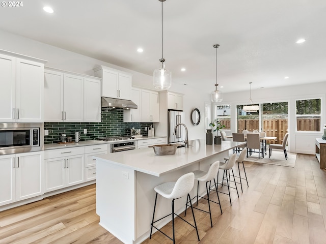 kitchen featuring a breakfast bar, stainless steel appliances, a kitchen island with sink, decorative light fixtures, and white cabinetry