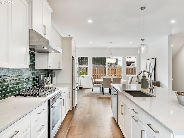 kitchen featuring appliances with stainless steel finishes, a kitchen island with sink, sink, white cabinetry, and hanging light fixtures