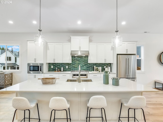 kitchen with stainless steel appliances, sink, pendant lighting, a center island with sink, and white cabinets