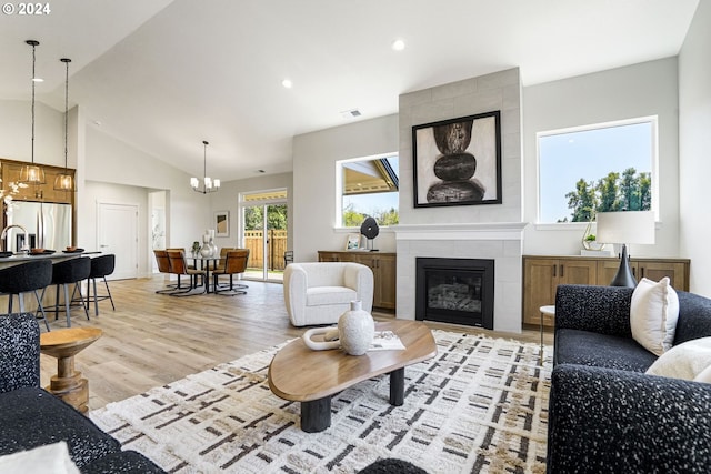 living room featuring a tiled fireplace, an inviting chandelier, vaulted ceiling, and light wood-type flooring