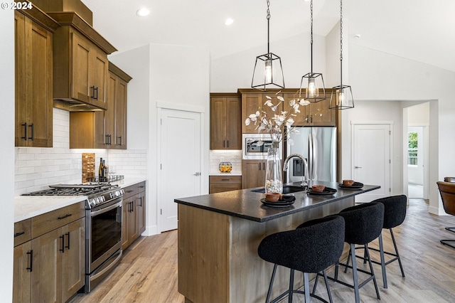 kitchen featuring appliances with stainless steel finishes, backsplash, pendant lighting, lofted ceiling, and an island with sink