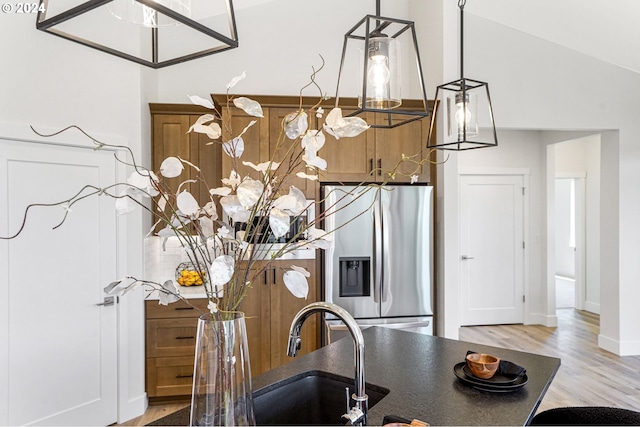 kitchen with stainless steel refrigerator with ice dispenser, vaulted ceiling, sink, hardwood / wood-style flooring, and decorative light fixtures