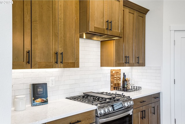 kitchen featuring decorative backsplash, light stone countertops, ventilation hood, and stainless steel gas range oven