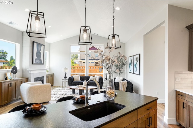 kitchen with hanging light fixtures, sink, a tile fireplace, and vaulted ceiling