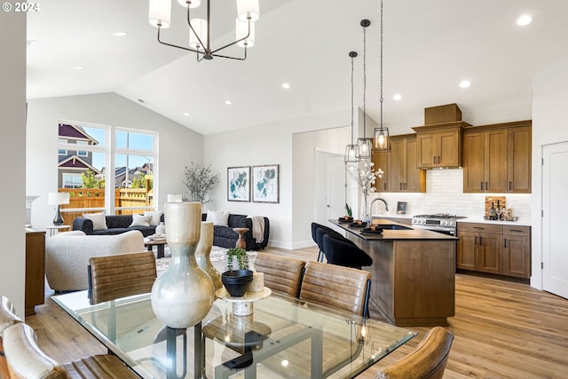 dining area with an inviting chandelier, light hardwood / wood-style flooring, vaulted ceiling, and sink