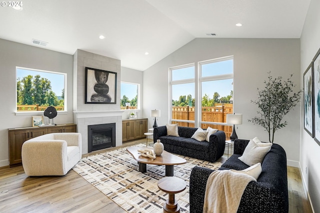 living room featuring vaulted ceiling, light wood-type flooring, and a tiled fireplace