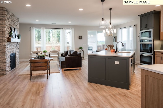 kitchen with pendant lighting, sink, light hardwood / wood-style floors, a kitchen island with sink, and a stone fireplace