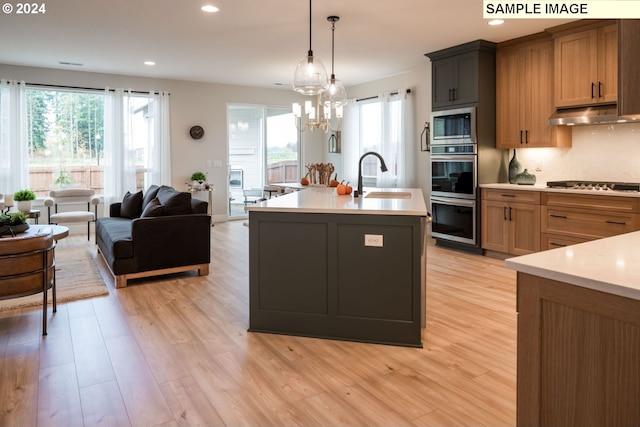 kitchen with sink, stainless steel appliances, light hardwood / wood-style flooring, hanging light fixtures, and a kitchen island with sink