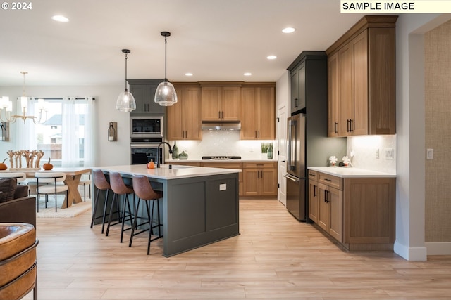 kitchen featuring light wood-type flooring, a kitchen island with sink, hanging light fixtures, and appliances with stainless steel finishes