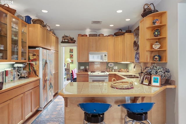 kitchen with tasteful backsplash, white appliances, a kitchen bar, sink, and kitchen peninsula