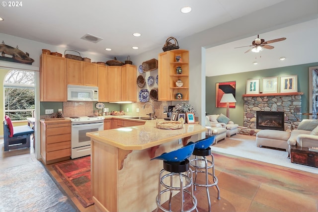 kitchen featuring tasteful backsplash, a breakfast bar, white appliances, a fireplace, and kitchen peninsula