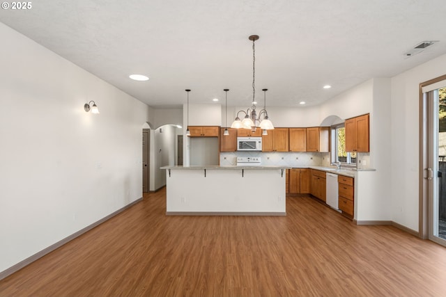 kitchen with light wood-type flooring, backsplash, white appliances, pendant lighting, and a center island