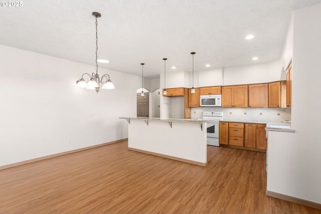 kitchen with white appliances, decorative light fixtures, wood-type flooring, a breakfast bar area, and a chandelier