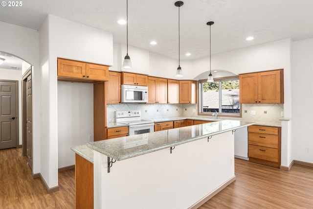 kitchen with light stone countertops, a kitchen island, hanging light fixtures, and white appliances